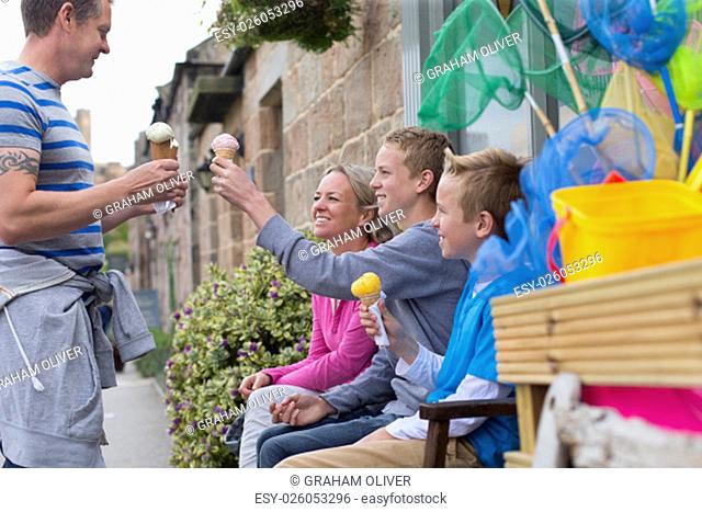 Family enjoying ice cream outside of a shop. They are all holding their cones and smiling