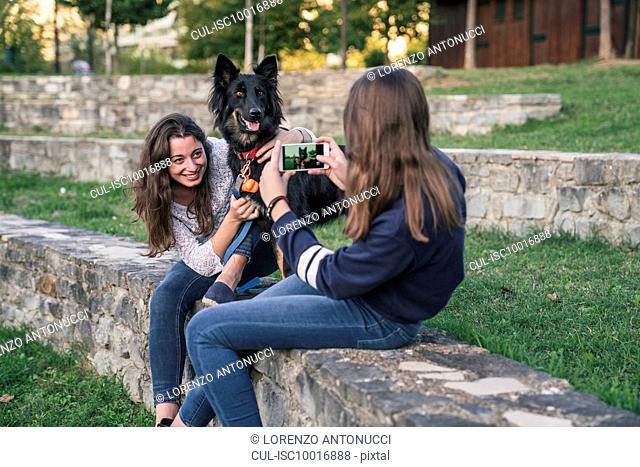 Sisters taking photograph with dog in park