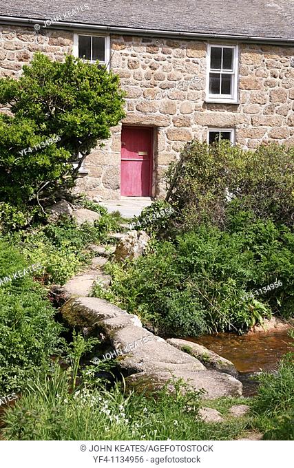 Old stone built cottage with a clapper bridge crossing the stream in front of it Cornwall, England