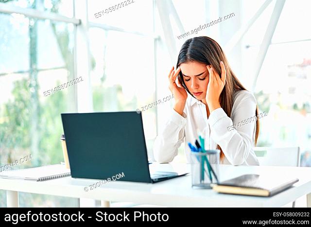 Stressed tired businesswoman sitting at her desk in modern office. Problems, pain concept