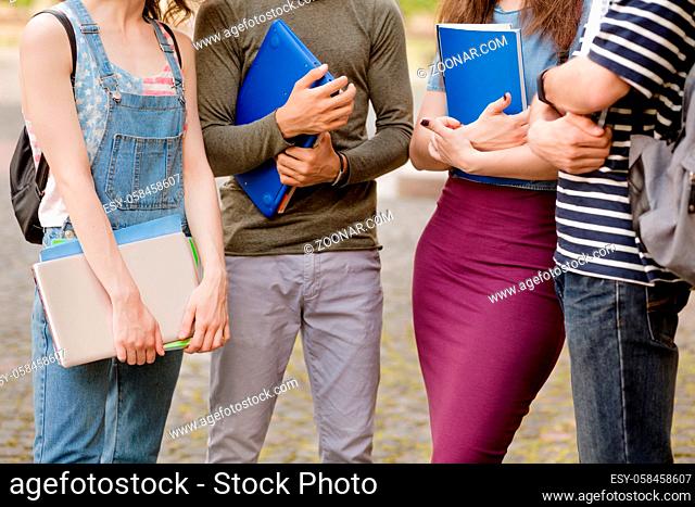 Students standing outside university holding textbooks in their arms. College friends standing together after classes