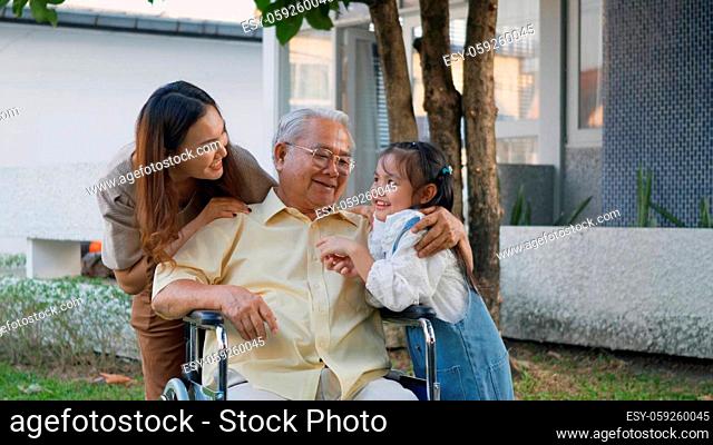 Disabled senior grandpa on wheelchair with grandchild and mother in park, Happy Asian three generation family having fun together outdoors backyard