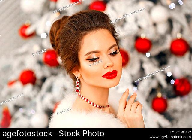 Elegant woman Cristmas portrait. Beautiful brunette lady with ruby jewelry set and wedding hairstyle, beauty makeup wears posing over xmas tree background