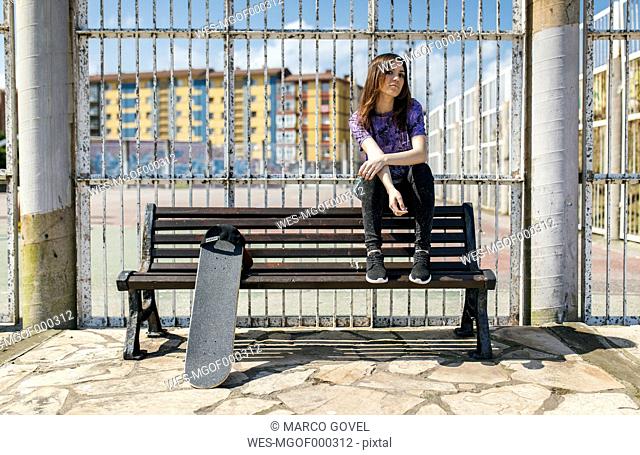 Spain, Gijon, female skate boarder sitting on backrest of a bench