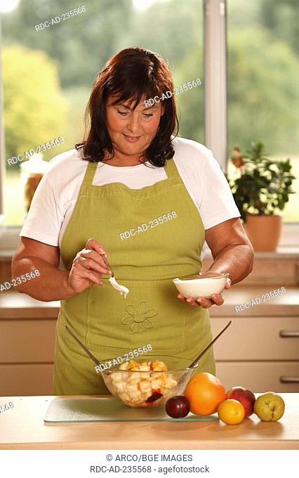 Woman preparing fruit salad with yoghurt / spoon, bowl