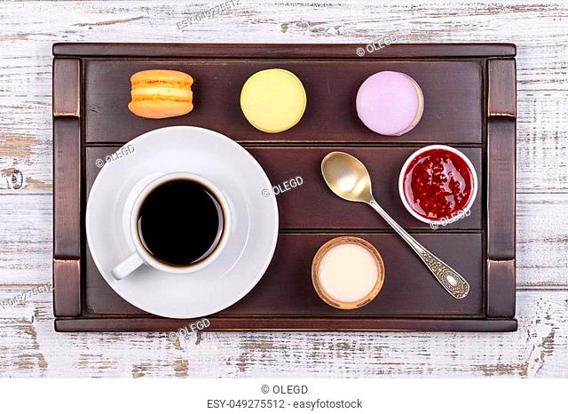Cup of coffee, spoon and macaron cakes on tray on white wooden table. Lifestyle concept. Close up. Top view