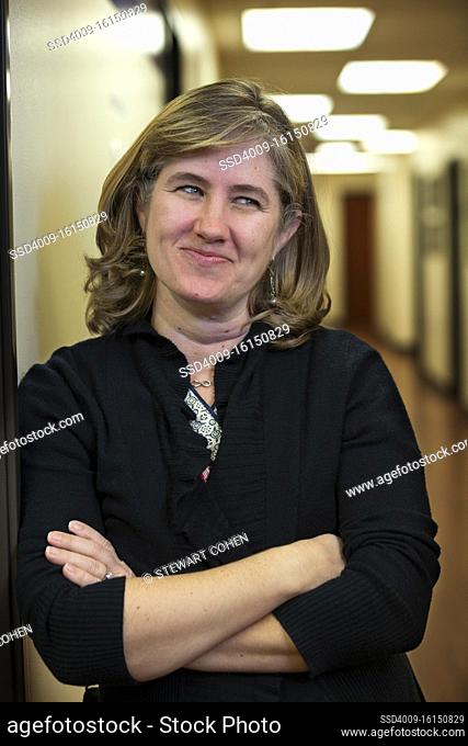 Portrait of middle aged woman with arms crossed in hallway of office building, smirking looking off camera