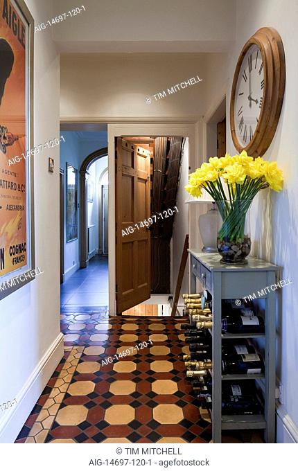 Daffodils and clock with wine storage in entrance hall of Macclesfield townhouse, Cheshire, England, UK