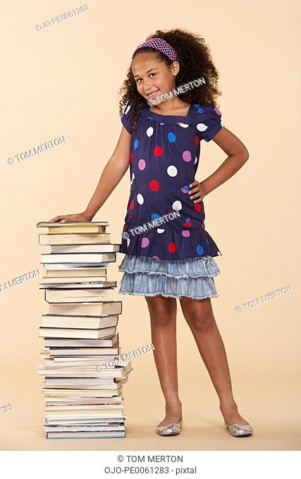 Young girl standing by a stack of books indoors