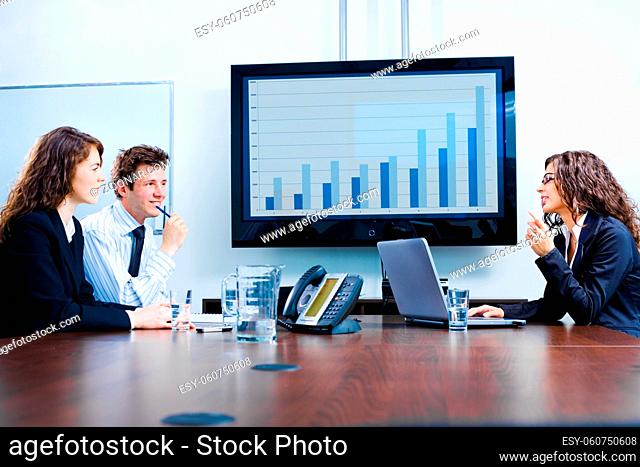 Happy young businesspeople having meeting in boardroom at office in front of a huge plasma TV screen, indoor, smiling