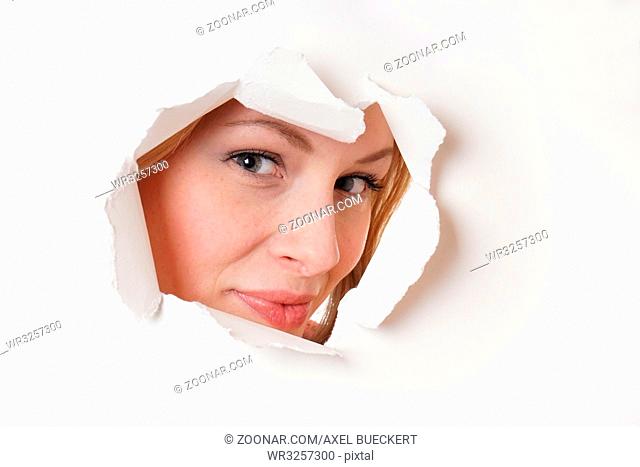smiling young woman peeking through hole in paper wall