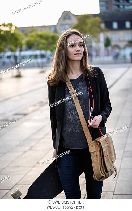 Young woman with longboard and cell phone in the city on the move
