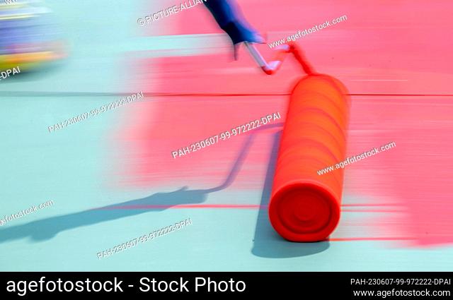 07 June 2023, Saxony, Chemnitz: A paint roller is used to apply red paint to the roof of the Stadthalle in Chemnitz. Pupils of the Chemnitz school model help...