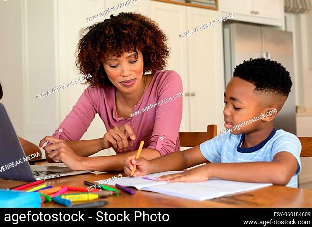 Happy african american mother and son doing homework at home smiling