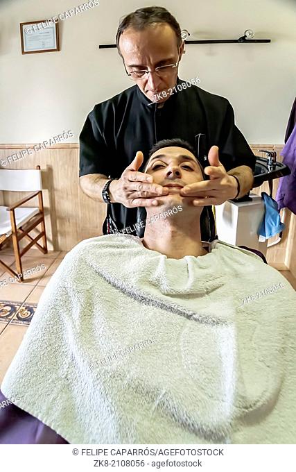 Barbero extends cream in the face of the client after shaver in a barber's shop, Sabiote, Jaen province, Andalucia, Spain