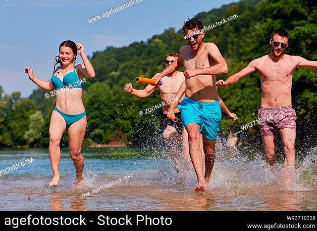 Summer joy group of happy friends having fun while running and splashing on river