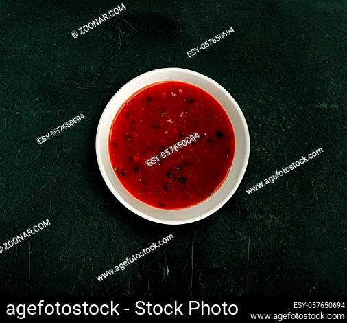 Flat lay, top view of a white porcelain or ceramic bowl of spice ketchup sauce isolated on dark green texture background