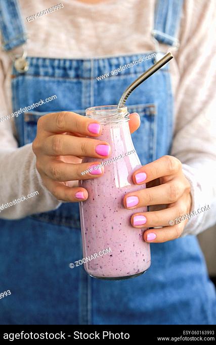 Female hands holding Blueberry smoothie topped with blueberries. Woman eating glass of breakfast protein smoothie drink made from pureed raw blueberries, banana