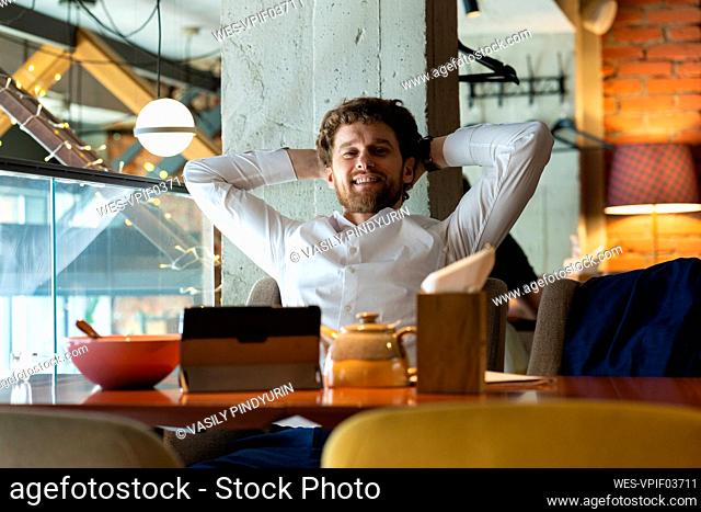 Relaxed businessman with hands behind head sitting at cafe