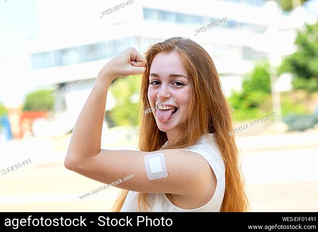 Businesswoman with bandage on arm sticking out tongue during pandemic
