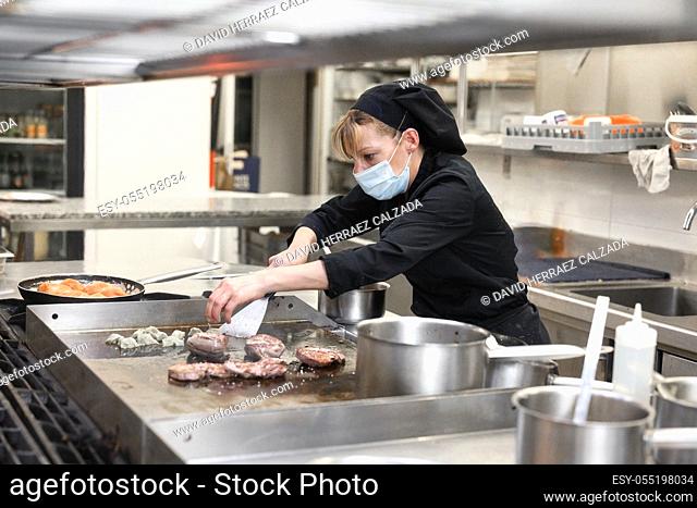 Woman Chef in protective face mask prepare food in the kitchen of a restaurant or hotel. Coronavirus prevention concept. High quality photo