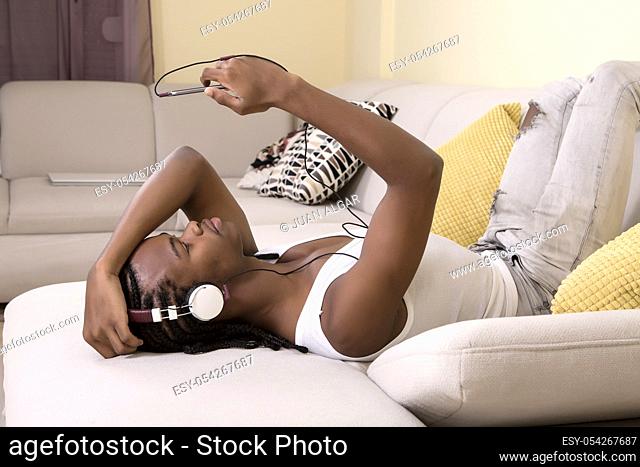 Young black man lying on sofa and enjoying the music with smartphone