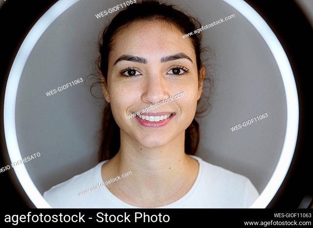 Young woman smiling while standing in front of circular flash against gray background