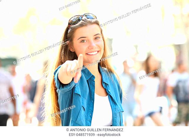 Single happy woman pointing and looking at camera standing in the street