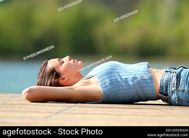 Side view portrait of a relaxed woman resting lying in a lake pier in summer vacation