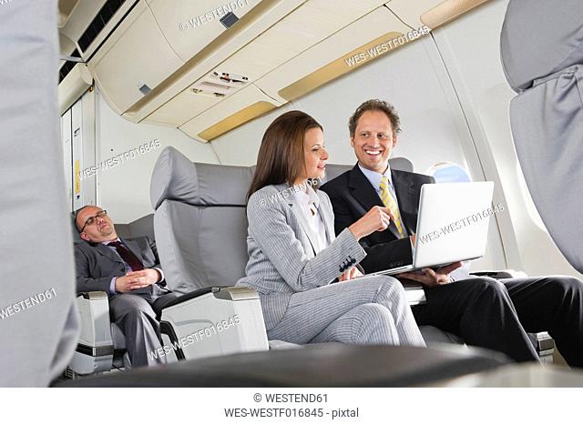 Germany, Bavaria, Munich, Businessman and businesswoman working on laptop in business class airplane cabin