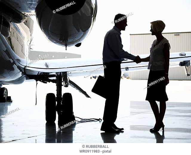 Profile of a businessman and a businesswoman shaking hands by an airplane