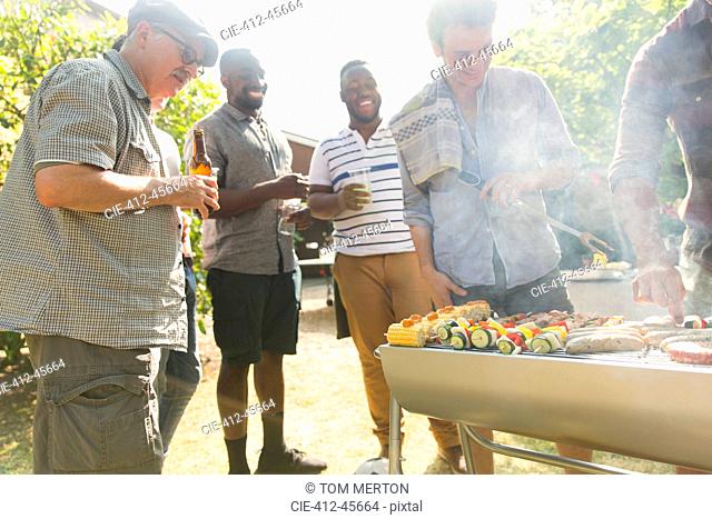 Male friends drinking beer around barbecue grill in backyard