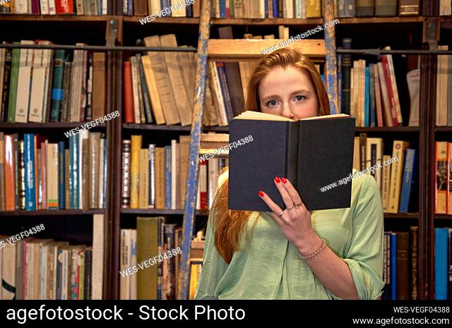 Young woman with book standing on ladder in library