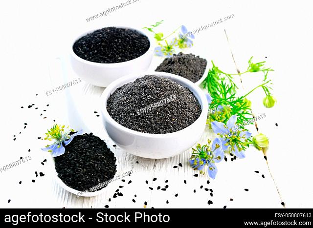 Flour and seeds of black caraway in bowls, sprigs of kalingini with blue flowers and green leaves on a white wooden board background