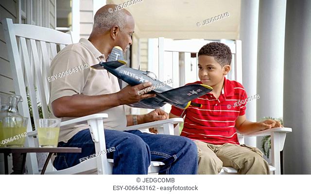 A grandfather and grandson examine a model airplane on the porch of a suburban home