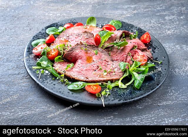 Modern style traditional Commonwealth Sunday roast with sliced cold cuts roast beef served with tomatoes and corn lettuce as close-up on a Nordic design plate