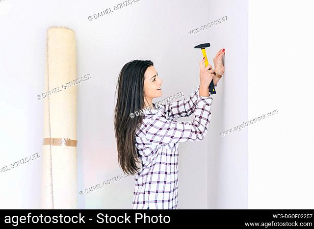 Smiling woman hammering nail in wall at home
