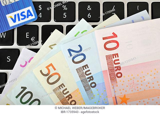 Fan of various euro banknotes and a VISA credit card on the keyboard of a laptop, PC, symbolic image for Internet businesses and computer businesses