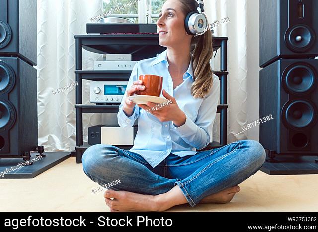 Woman drinking coffee and listening to music sitting on the floor of her home