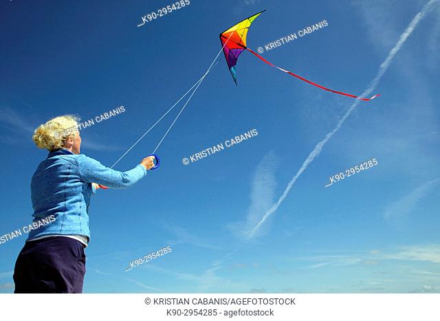 Young caucasian woman letting her kite fly with blue sky, Amrum, Northfrisian, Schleswig-Holstein, Germany, Europe