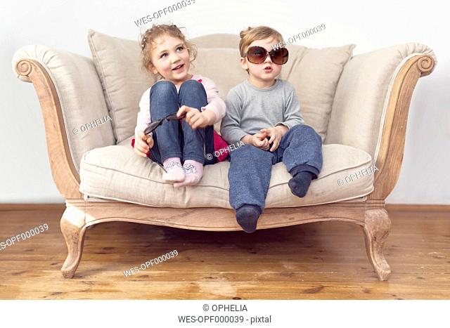Brother and sister with oversized sunglasses sitting on couch