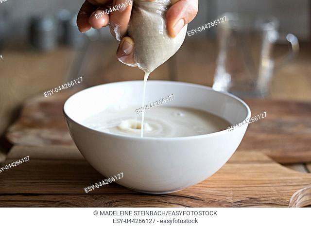 Preparation of nut milk - straining the milk through a milk bag into a bowl