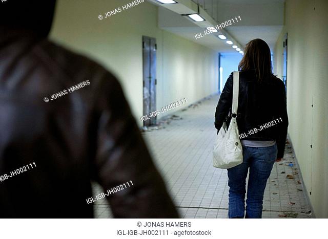 This picture shows a man following a woman in a covered passage as he tries to rape or steal the bag