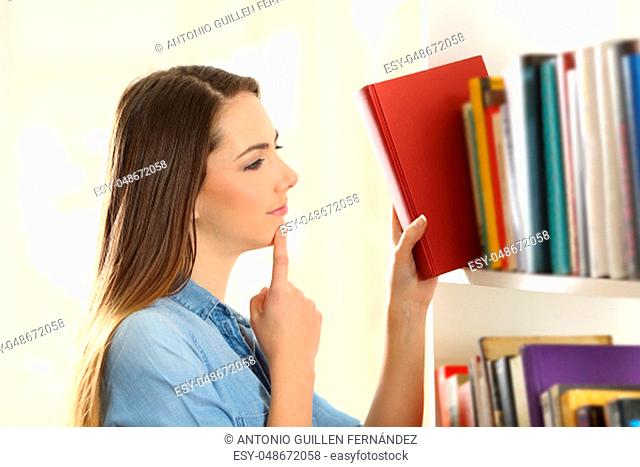 Pensive woman choosing a book from shelving at home