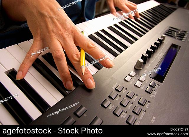 Woman's fingers with pencil on digital piano keys
