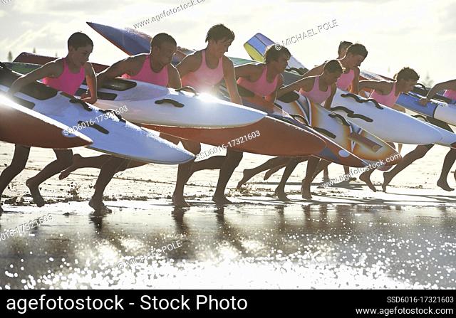 Team of male surf lifeguards training and running into sea holding ocean surf skis