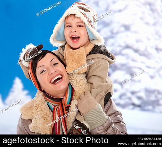 Portrait of happy mother and child together in snow on a cold winter day laughing, smiling