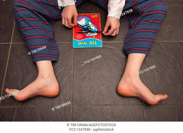 A boy practises tying shoelaces on a learning card by orchard toys in the Uk