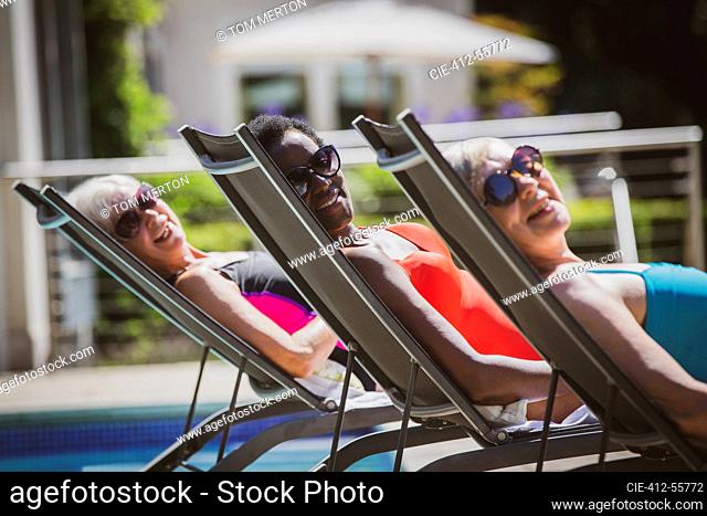 Portrait carefree senior women friends sunbathing at sunny poolside