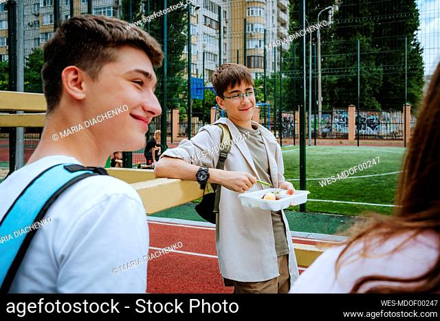 Smiling boy with lunch box standing with friends in schoolyard
